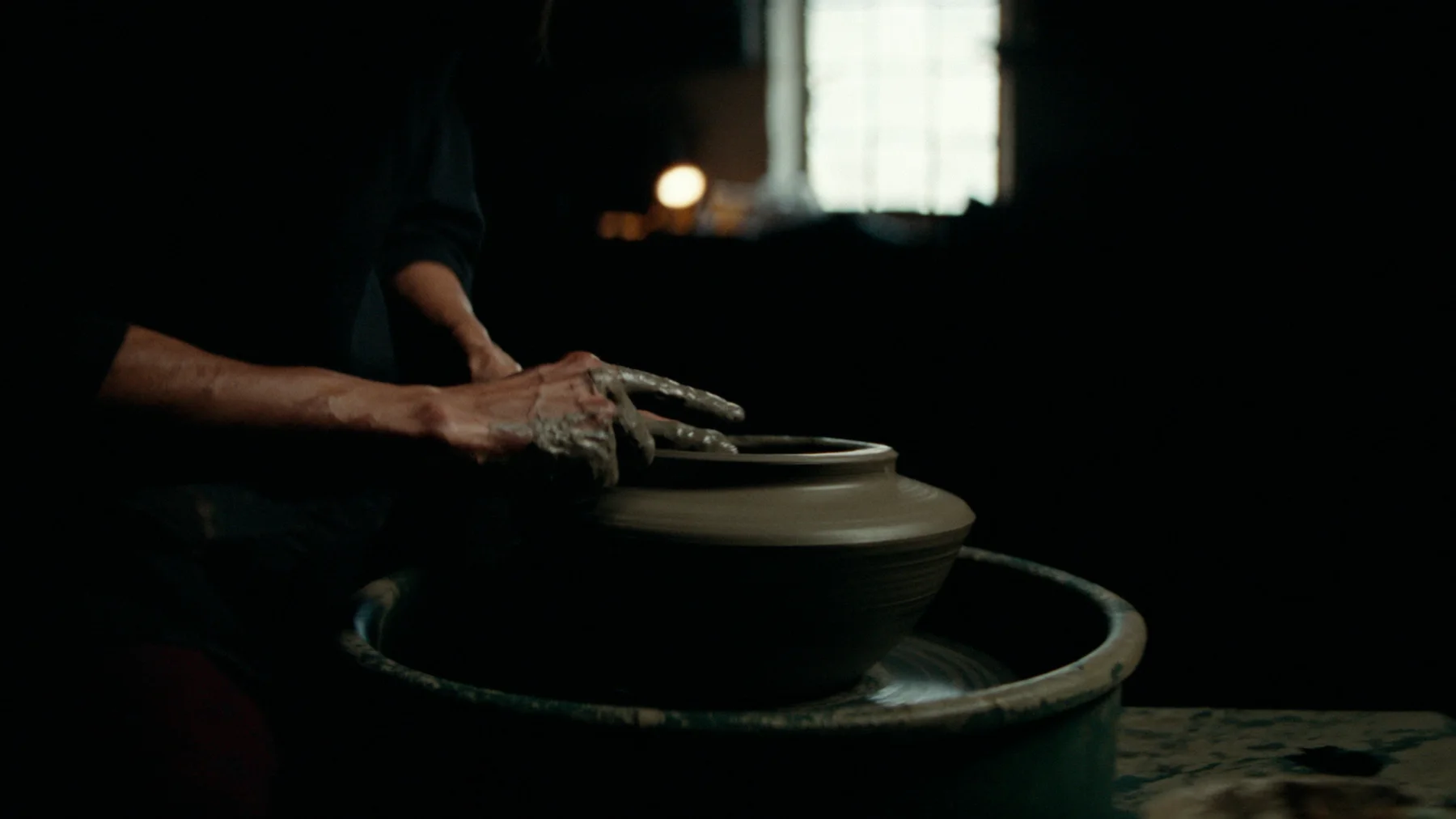 A potter's hands centering wet clay on a spinning wheel.