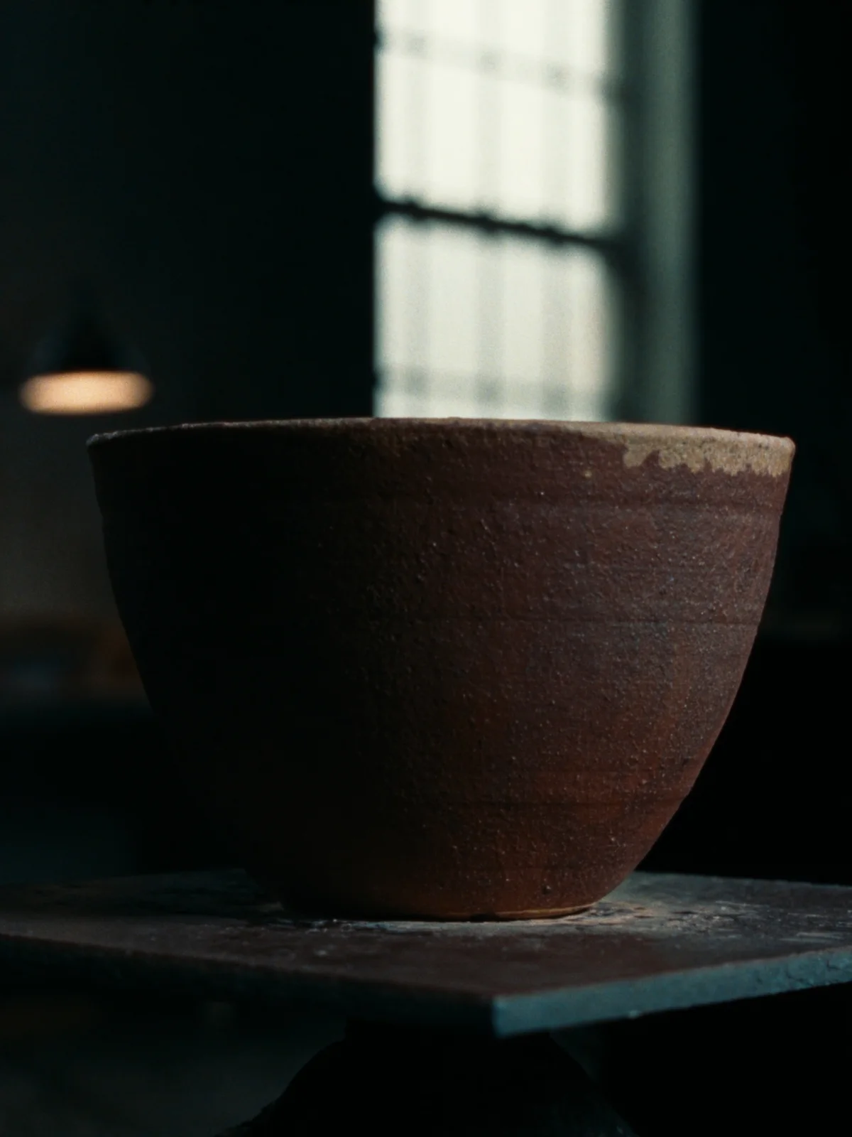 A wide stoneware cup with a bare iron-red clay body and an ash-glazed rim.